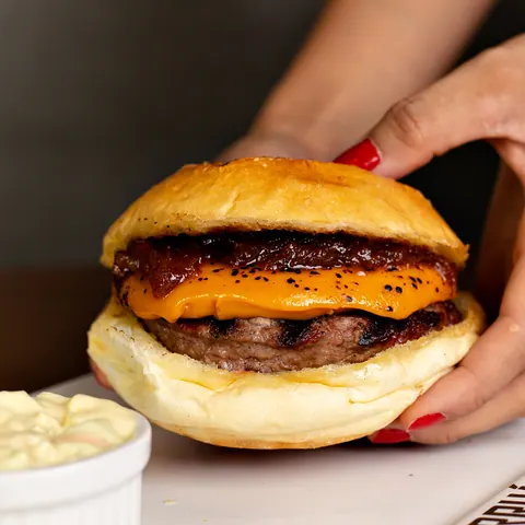 Mão segurando hambúrguer com cheddar em pão macio
