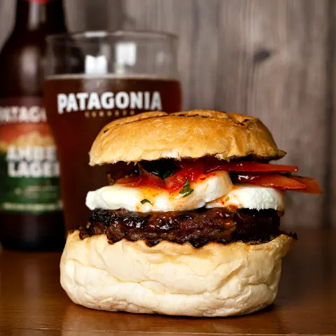 Hambúrguer com mussarela e tomate ao lado de uma cerveja