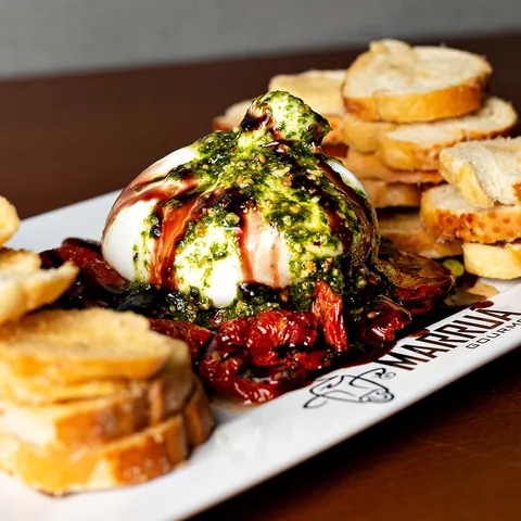 Burrata com pesto e tomate seco, acompanhada de torradas