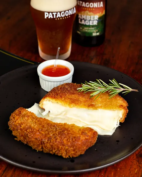 Queijo empanado com molho de pimenta e cerveja artesanal ao fundo