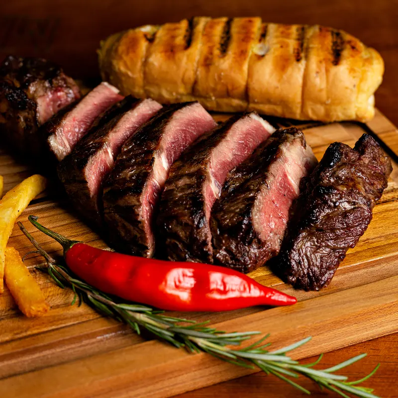 Steak fatiado ao ponto sobre tábua, com pão de alho e pimenta