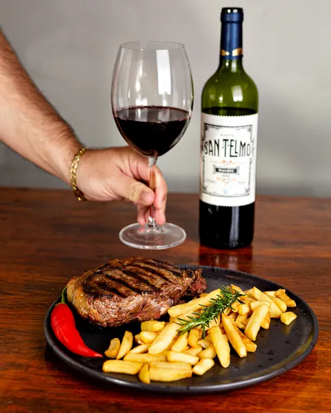 Taça de vinho tinto ao lado de um steak com fritas